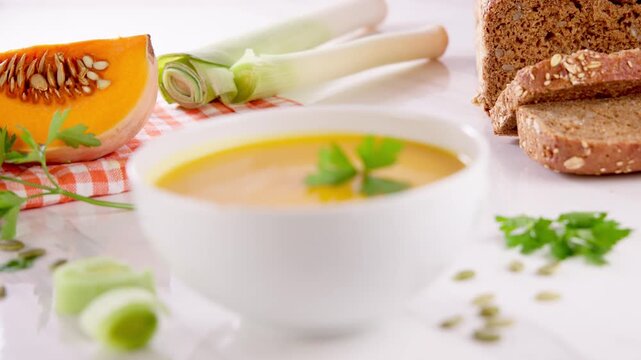 bowl of warm pumpkin soup served with sliced rye bread leek and fresh ingredients