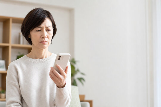 自宅でスマートフォンを見て不安になる中年女性