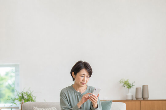 自宅のソファでスマートフォンを操作する中年女性