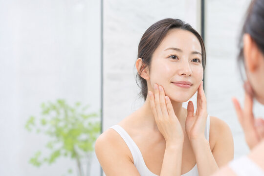 明るい洗面所で肌を確認する笑顔の女性