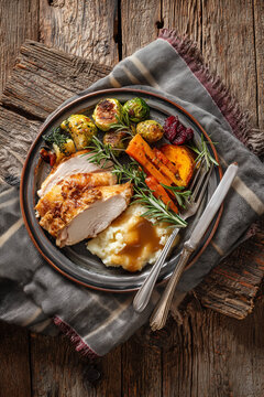 Thanksgiving Plate with Turkey Breast, Mashed Potatoes and Gravy Surrounded by Roasted Vegetables on a Rustic Wood Table