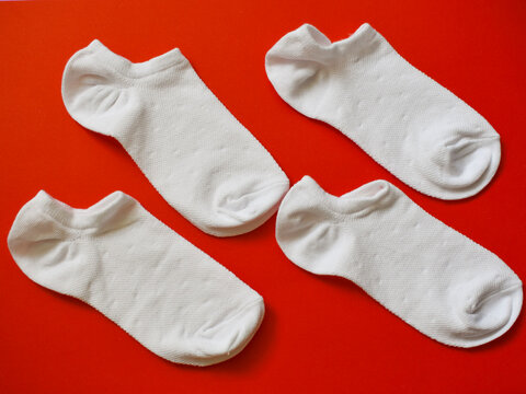 White low cut ankle socks arranged neatly on vibrant bright red paper background surface in top view flat lay composition layout