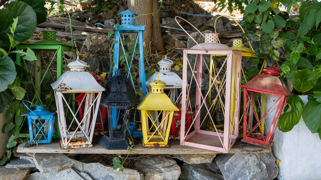 Colorful decorative lanterns arranged outdoors among green foliage and stones   