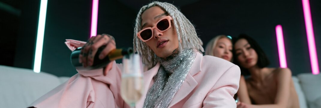 Glamorous party portrait with neon lights and champagne in a pink suit for nightclub banner and fashion background