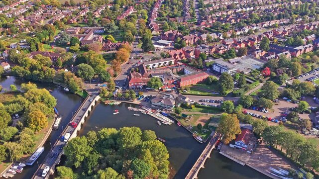 Clopton Bridge with traffic beside moored rowing boats, jetties and red brick riverside buildings on the River Avon in Stratford upon Avon, Warwickshire, aerial descent