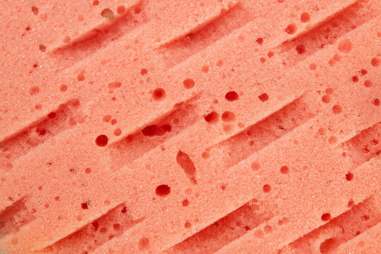 Macro texture background of a porous pink foam sponge with diagonal ribbed lines