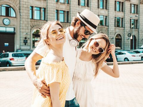 Group of young three stylish friends posing in the street. Fashion man and two cute dressed in casual summer clothes. Smiling models having fun near wall.Cheerful women and guy outdoors