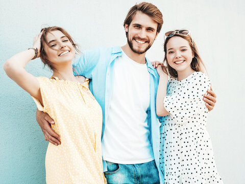 Group of young three stylish friends posing in the street. Fashion man and two cute dressed in casual summer clothes. Smiling models having fun near wall.Cheerful women and guy outdoors