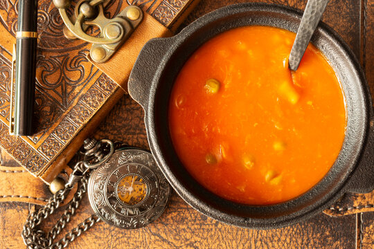 Bowl of vegetable soup with a vintage leather journal, fountain pen and a pocket fob watch on an aged leather background backdrop