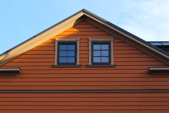 modern wooden house with orange plank facade and two small windows on the attic