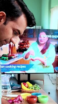 Young Indian man learning to prepare traditional modak dumplings in a modern kitchen while watching a cooking recipe on TV, Indian cuisine, homemade food and culinary skills concept.
