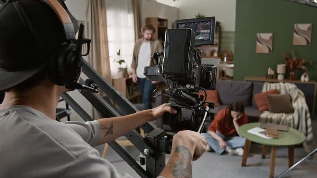 Caucasian cameraman operating professional cinema camera on crane while filming actors on movie set. Perfect for filmmaking masterclasses, media production marketing and backstage content
