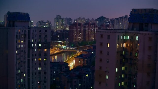 Residential towers frame a brightly illuminated street in Shanghai after sunset, with lit windows, warm streetlights and distant apartment blocks showing the dense layout of the city neighborhood.