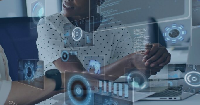 Leaning woman in polka-dot blouse working on laptop and documents in modern office with HUD