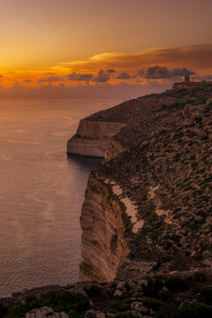 View of Steep Dingli Cliffs Dropping into the Calm Sea under Glowing Orange Sunset Sky, Malta