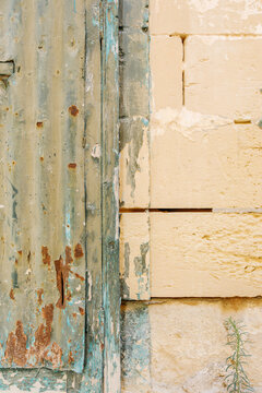 Old turquoise metal door with rust and peeling paint beside a weathered beige limestone wall