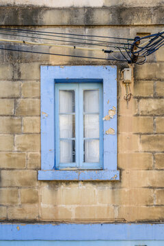 Light Blue Painted Wooden Window with Peeling Architrave Frame Set in Yellow Limestone Wall
