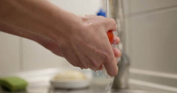 Close-up male hand wash rinse tomato under tap water in sink. 4K 10-bit