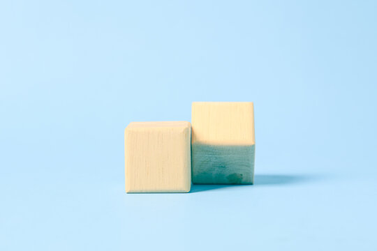 Two blank natural wooden blocks standing side by side at different heights on a clean pastel blue background, offering a minimal concept for comparison, business foundations, balance.