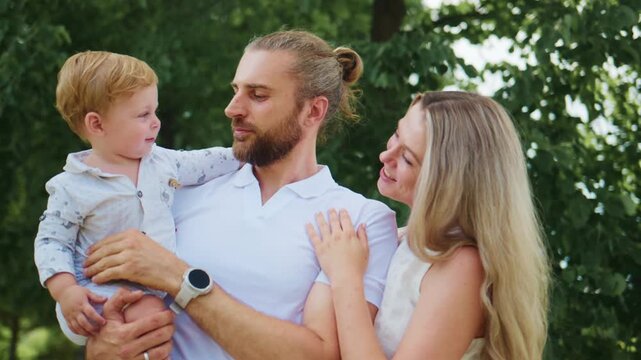 Happy family enjoying outdoor time together in a green park. Father holds toddler, mother smiles beside them. All look joyful, connected, and relaxed. Perfect for family, parenting