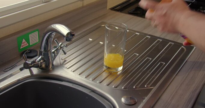Shot of orange squash cordial being made in a glass on the kitchen sink.