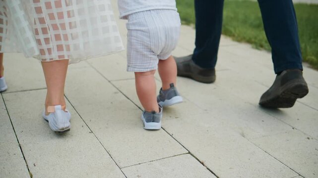 Child walks beside adults on paved path. Family strolls together outdoors. Moments of carefree childhood. Ideal for parenting, family, or lifestyle content. Natural daylight enhances warm