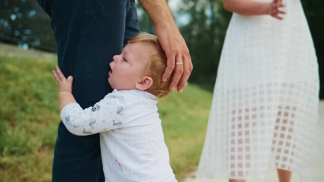Blond toddler reaches up to adults holding hands. Baby looks up with curiosity. Family moment outdoors on sunny day. Footage captures childhood innocence and connection. Ideal for parenting, family