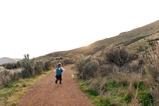Child running down a dirt path with bubbles at sunset