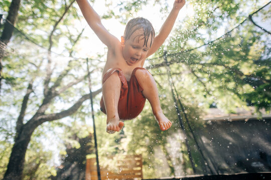 Young boy shouting with joy while jumping on a wet trampoline