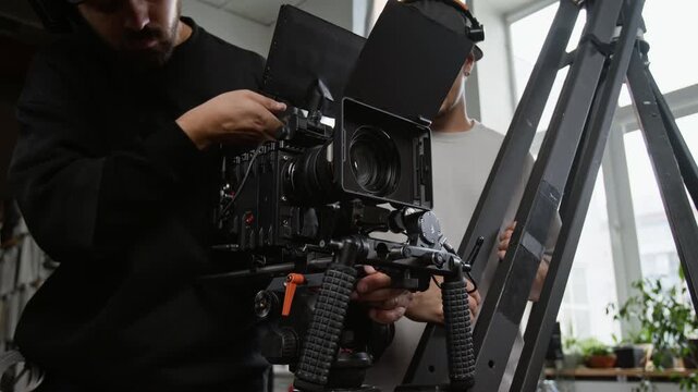 Two Caucasian young adult filmmakers mounting professional digital cinema camera on jib crane in studio. Footage ideal for media production commercials and filmmaking masterclass promotions