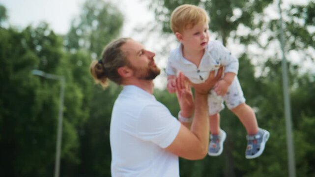 Father lifts toddler into air, both smiling. Child's joyful expression shows pure delight. Parent's gentle touch highlights tender bond. Perfect for family, parenting, or childhood themes