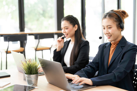 Two Asian Female Call Center Agents Wearing Headsets and Working on Laptops