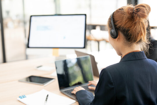 Back View of Call Center Agent Wearing Headset and Typing on Laptop at Office Desk