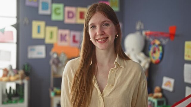 Woman teacher smiling with bare collarbone and open shirt, long hair over shoulder, in classroom building surrounded by toys and alphabet posters; learning warmth.