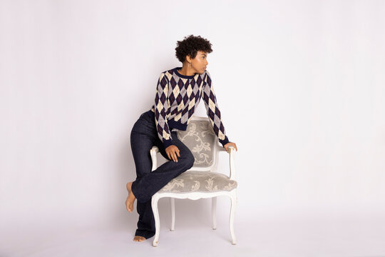 Hispanic woman posing in argyle sweater and jeans on patterned chair