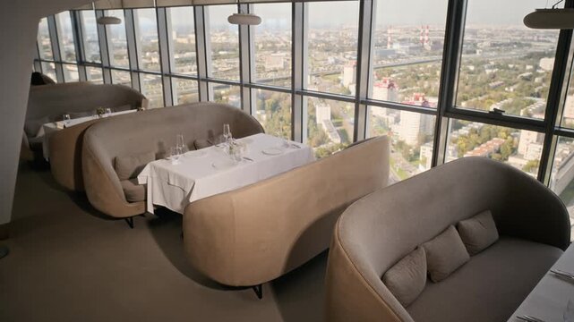 Empty served tables standing by panoramic skyscraper windows overlooking city skyline in luxury rooftop restaurant. Footage suitable for fine dining advertising and hospitality marketing