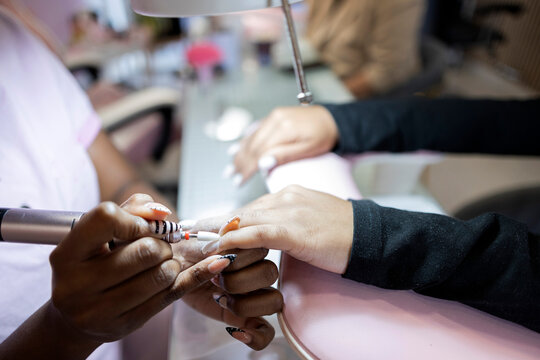 Manicurist shaping a client's nails with an electric nail file