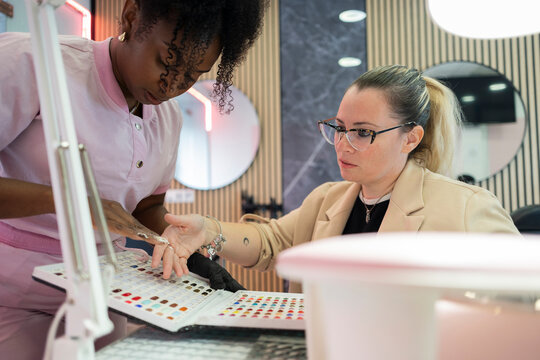 Client choosing nail polish with manicurist in beauty salon