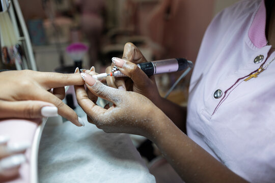 Nail technician shaping a client's manicure with an electric file