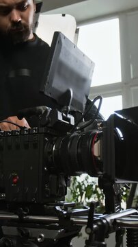 Vertical video of Caucasian young adult cameraman operating cinema camera rig on set. Footage suits video production advertising, cinematography tutorials, and filmmaking promos