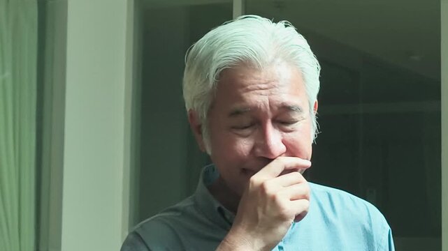 50s southeast asian man with white hair suffering a runny nose from cold or flu, home indoor scene