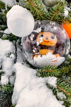 A Christmas tree is covered in ornaments and snow. A decoration inside a glass ball adds to the holiday spirit. It is winter and the ground is white