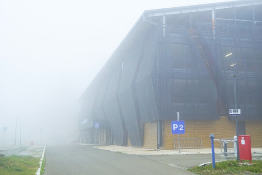 Modern angular parking garage with perforated metal facade, timber panels, and P2 sign emerging from thick mist. Illustrates contemporary resort infrastructure, ski facility, and low-cloud weather.