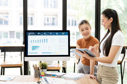 Two Asian Businesswomen Smiling and Using Digital Tablet in Office Meeting