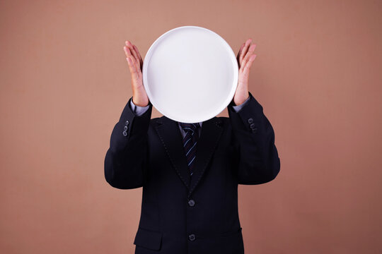 Man in Suit Holding Empty Dish Round Plate in Front Head Against Brown Background
