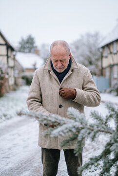 Senior man buttoning his warm wool coat while standing outdoors in a snow covered historic village during a cold winter day