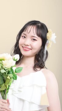 白いウェディングドレスを着てブーケを持つカメラ目線の若い20代の日本人女性の花嫁、結婚式やフォトウェディングの幸せと喜びを表現したブライダルイメージの縦動画