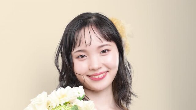 白いウェディングドレスを着てブーケを持つカメラ目線の若い20代の日本人女性の花嫁、結婚式やフォトウェディングの幸せと喜びを表現したブライダルイメージの動画