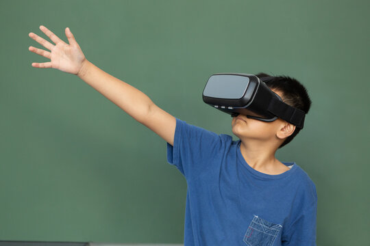 Schoolboy using virtual reality headset against greenboard in a classroom