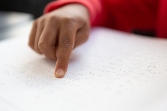 Person reading braille text with fingertip, wearing red sleeve